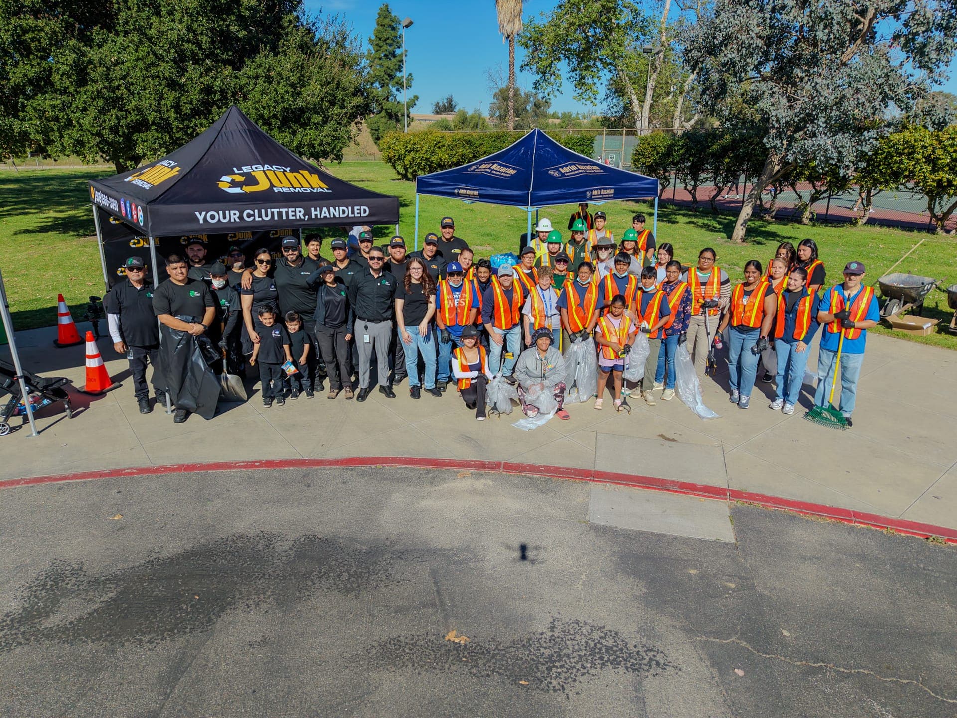 Drone view of the Legacy crew and dozens of volunteers in safety vests at a community clean-up, gathered by the Legacy canopy