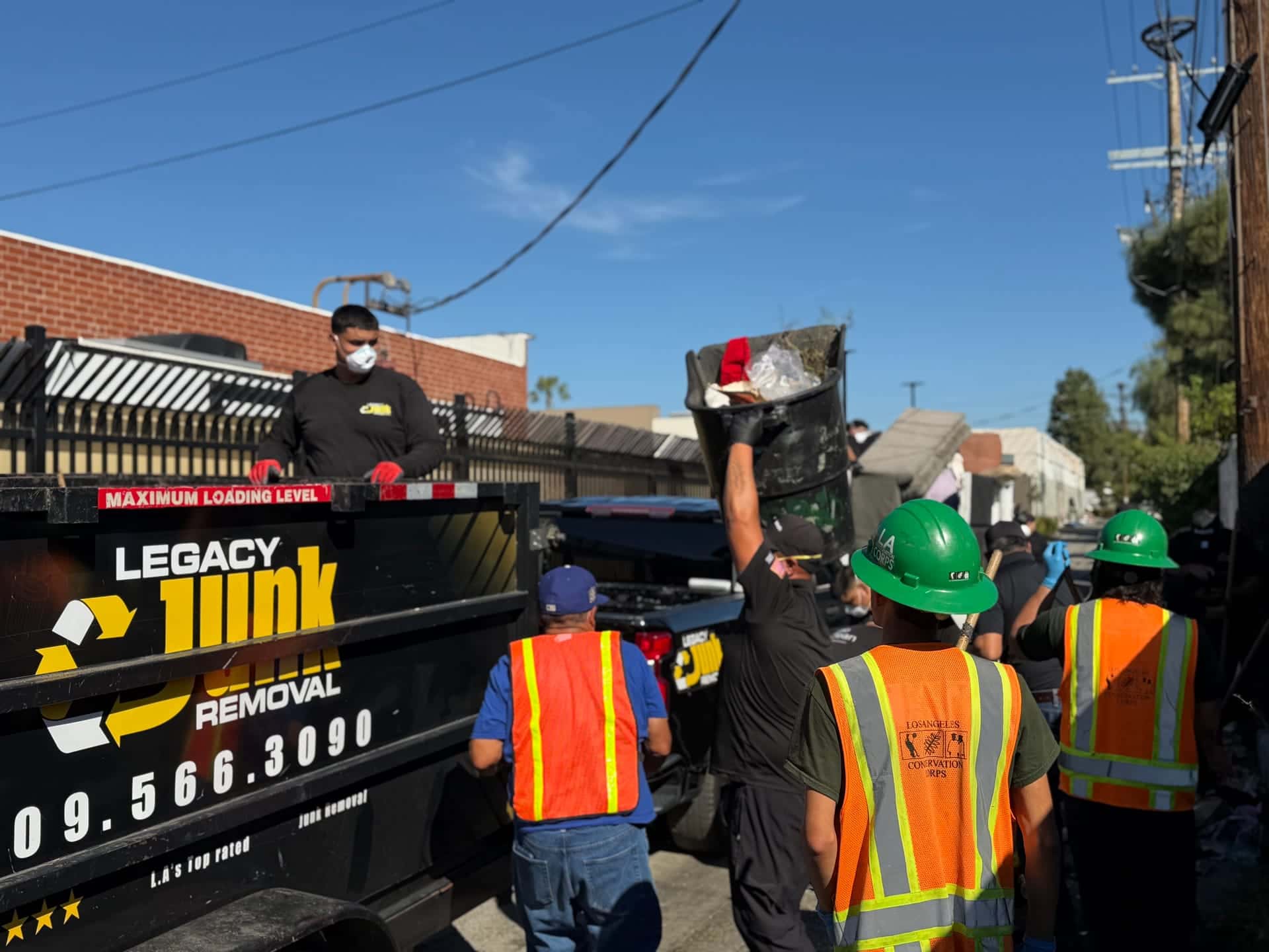 A Legacy crew member standing in the Legacy trailer while volunteers hand up bags and debris at a community clean-up