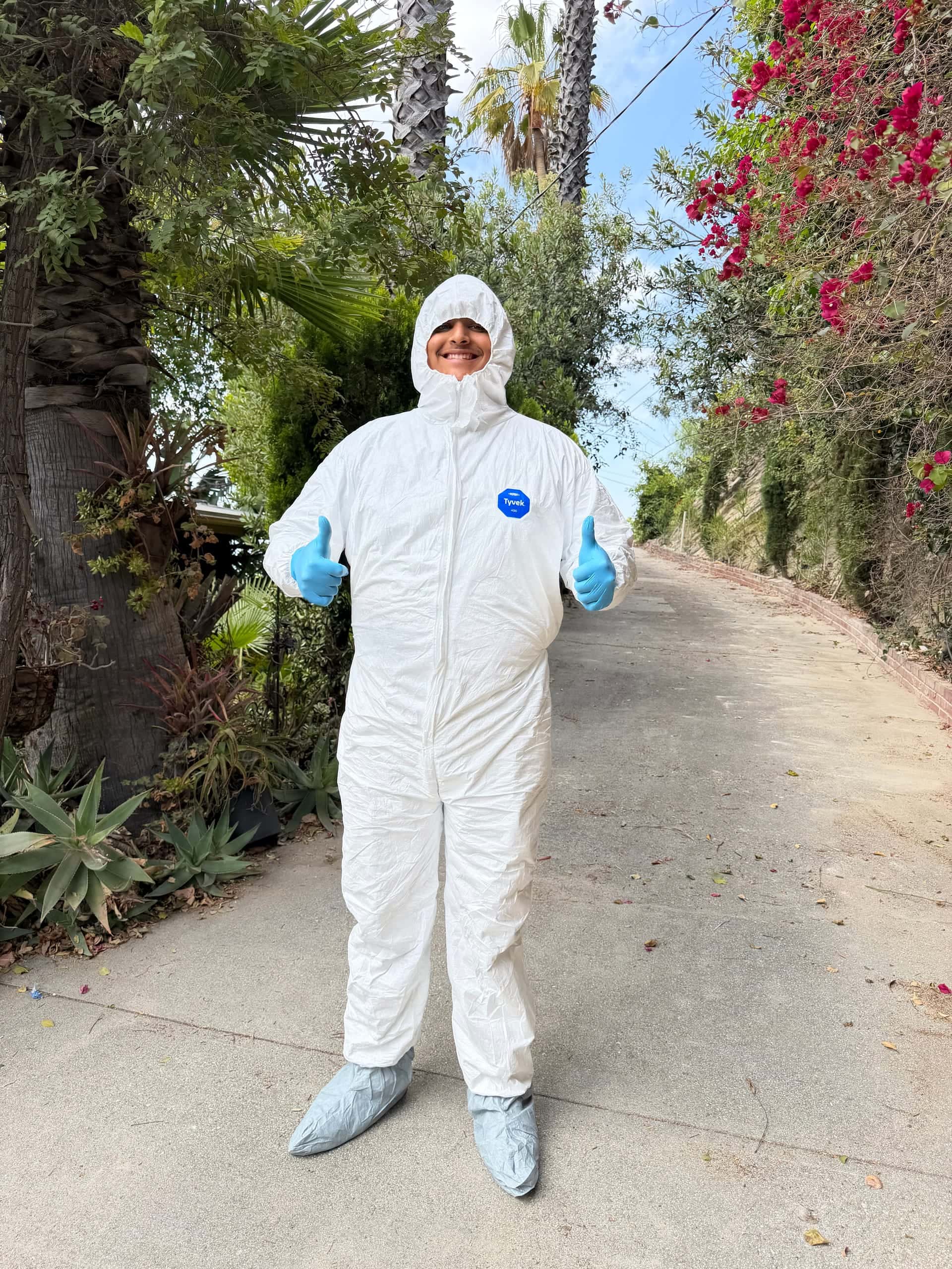 A Legacy crew member in a white protective suit, gloves and shoe covers giving two thumbs up