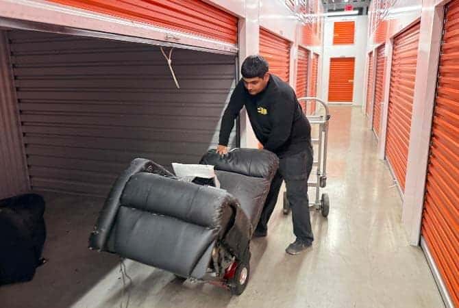 A Legacy crew member wheeling a leather recliner down a storage facility hallway