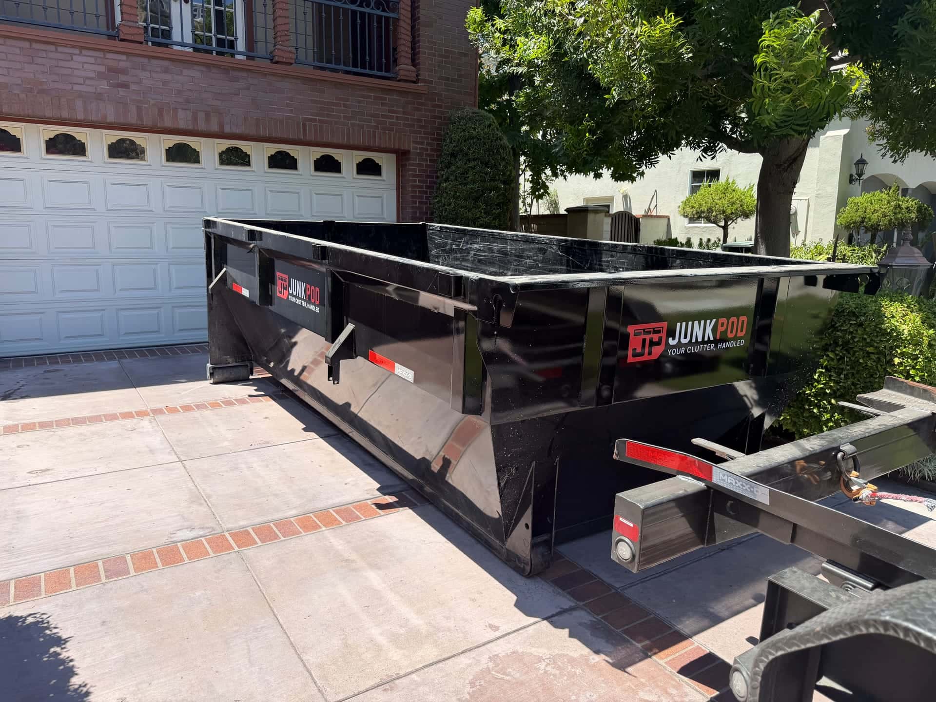 A black Legacy dumpster in the driveway of a brick house, in front of the garage door