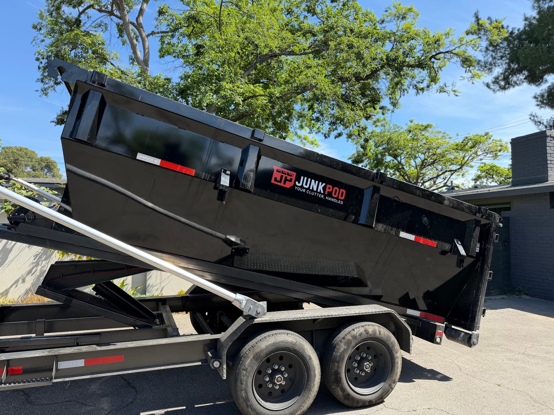 A black Legacy roll-off dumpster tilting off its delivery rig onto a driveway