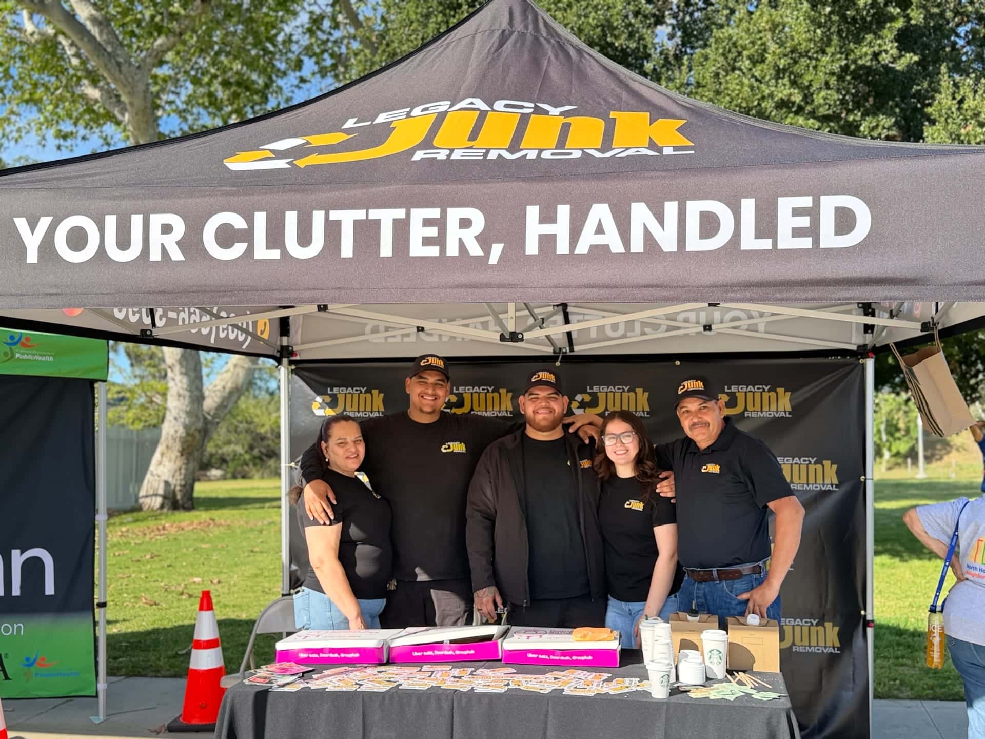 Five members of the Legacy family in Legacy shirts and caps at their booth under the black "Your clutter, handled" canopy