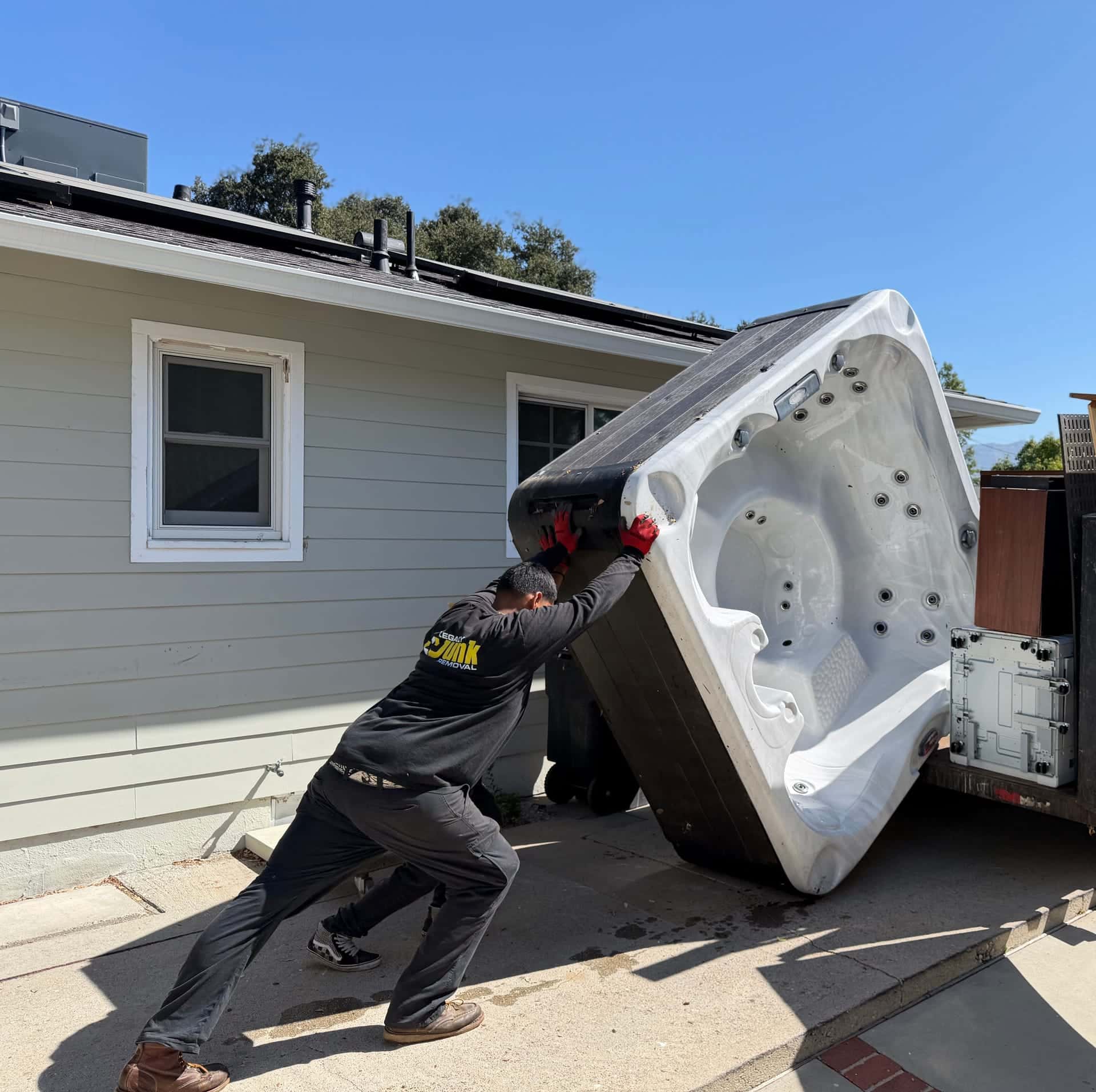 A Legacy crew member pushing an old spa shell up onto the trailer beside a house