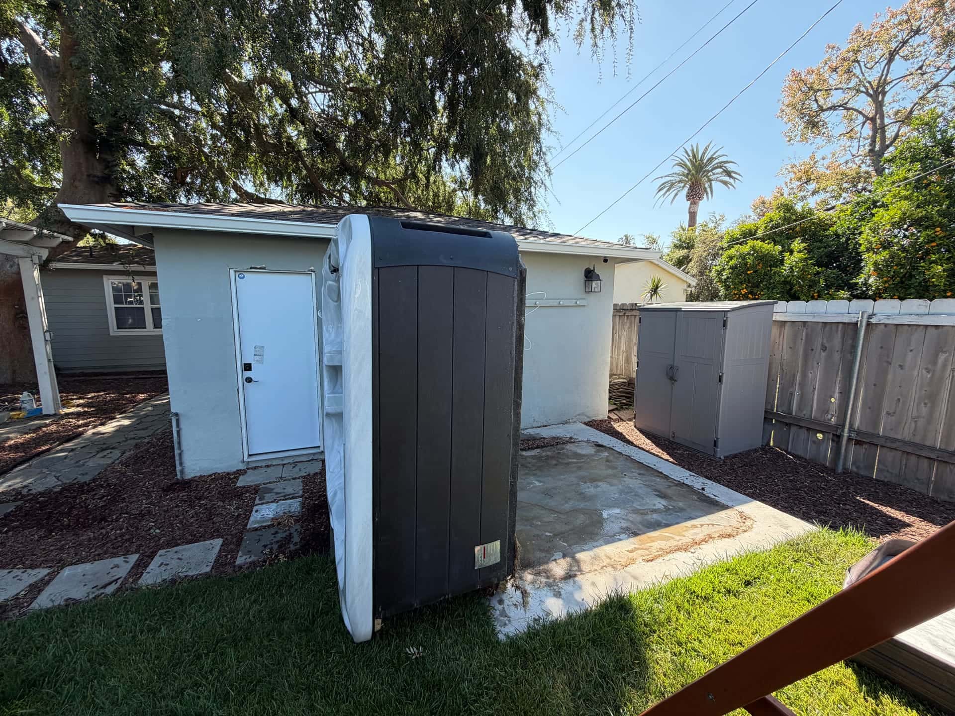 An old hot tub stood on its side in a backyard, ready to be carried out