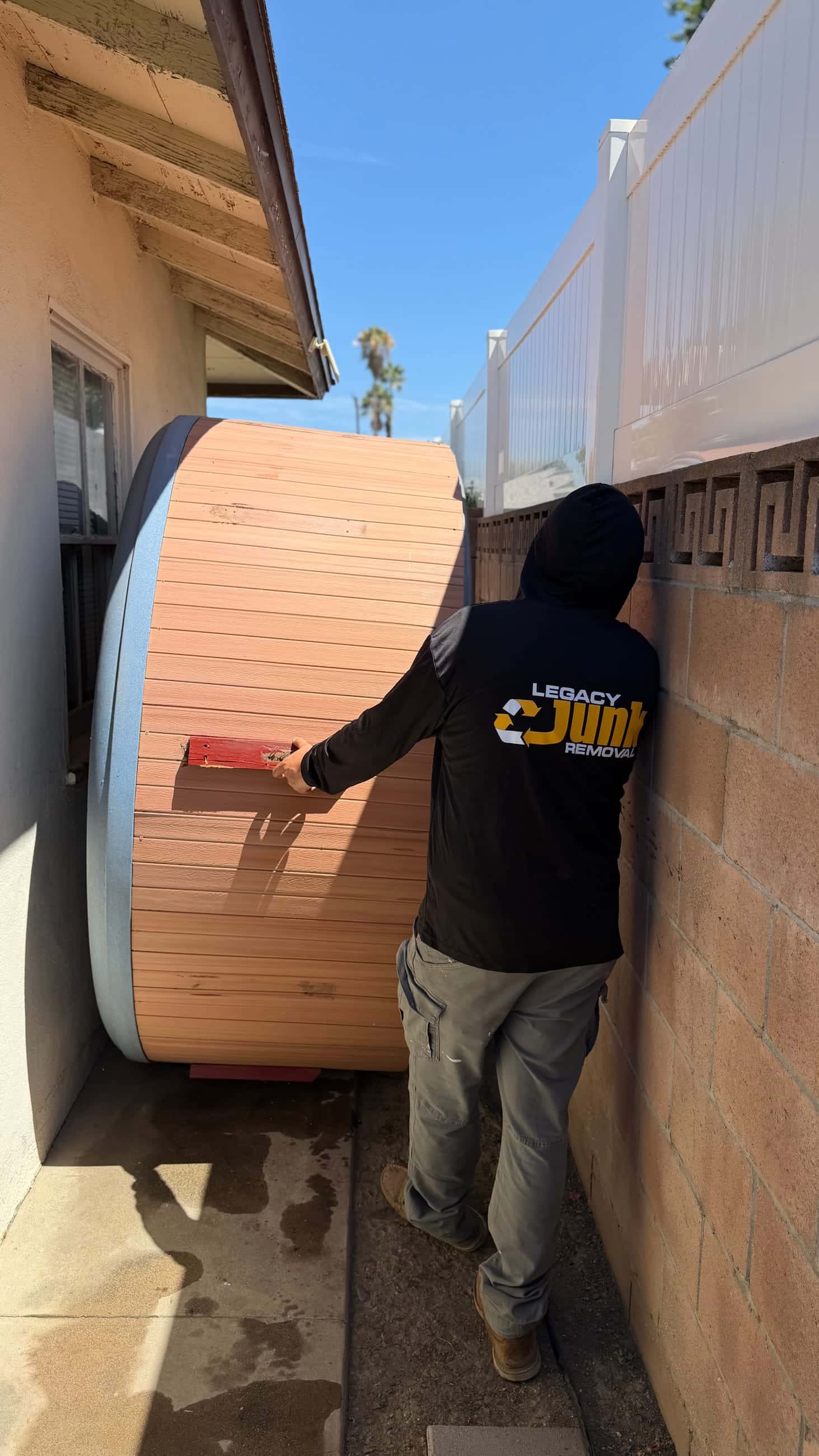 A Legacy crew member walking a hot tub on its side through a narrow side yard