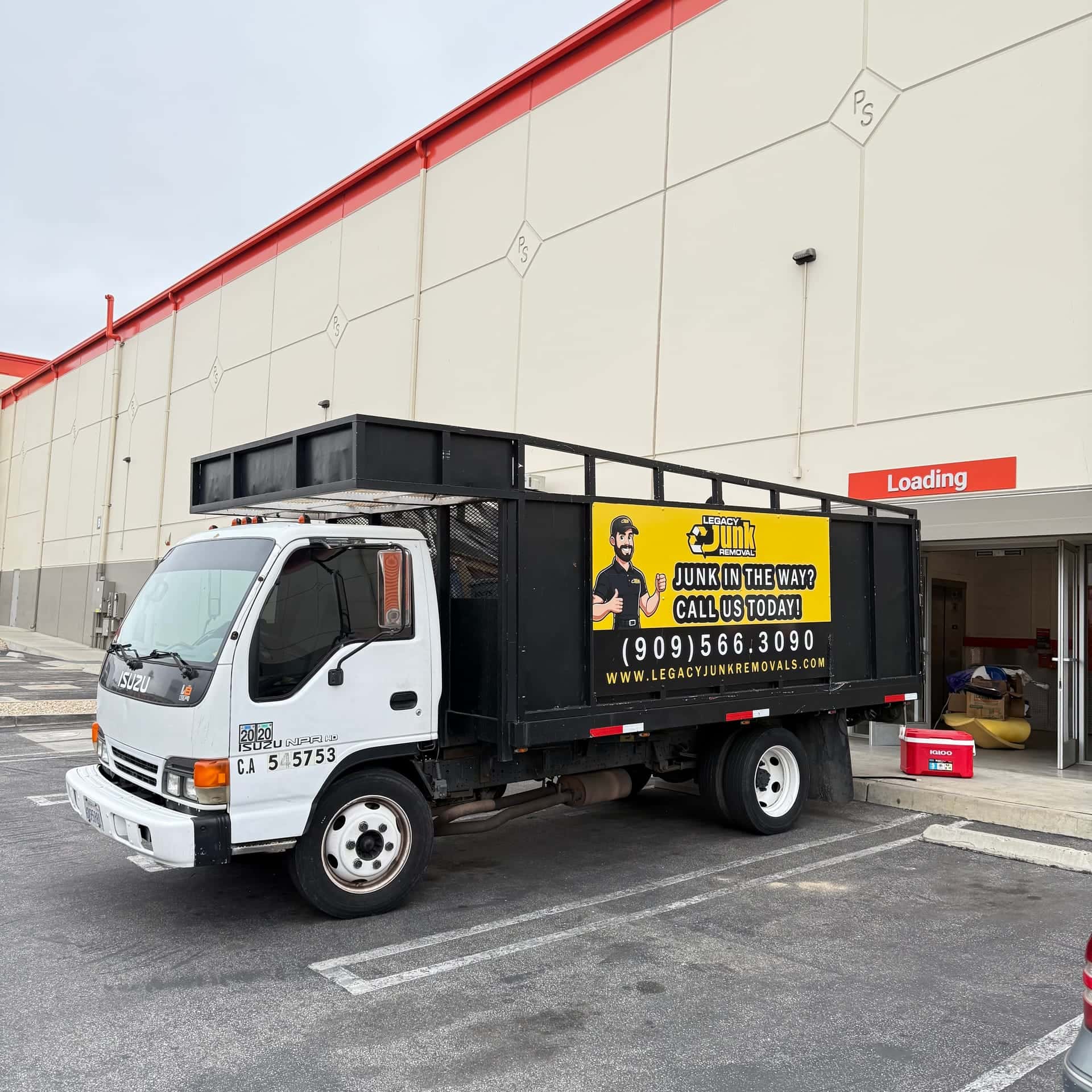 Legacy's white cab-over truck with its yellow and black wrap, parked at a loading door