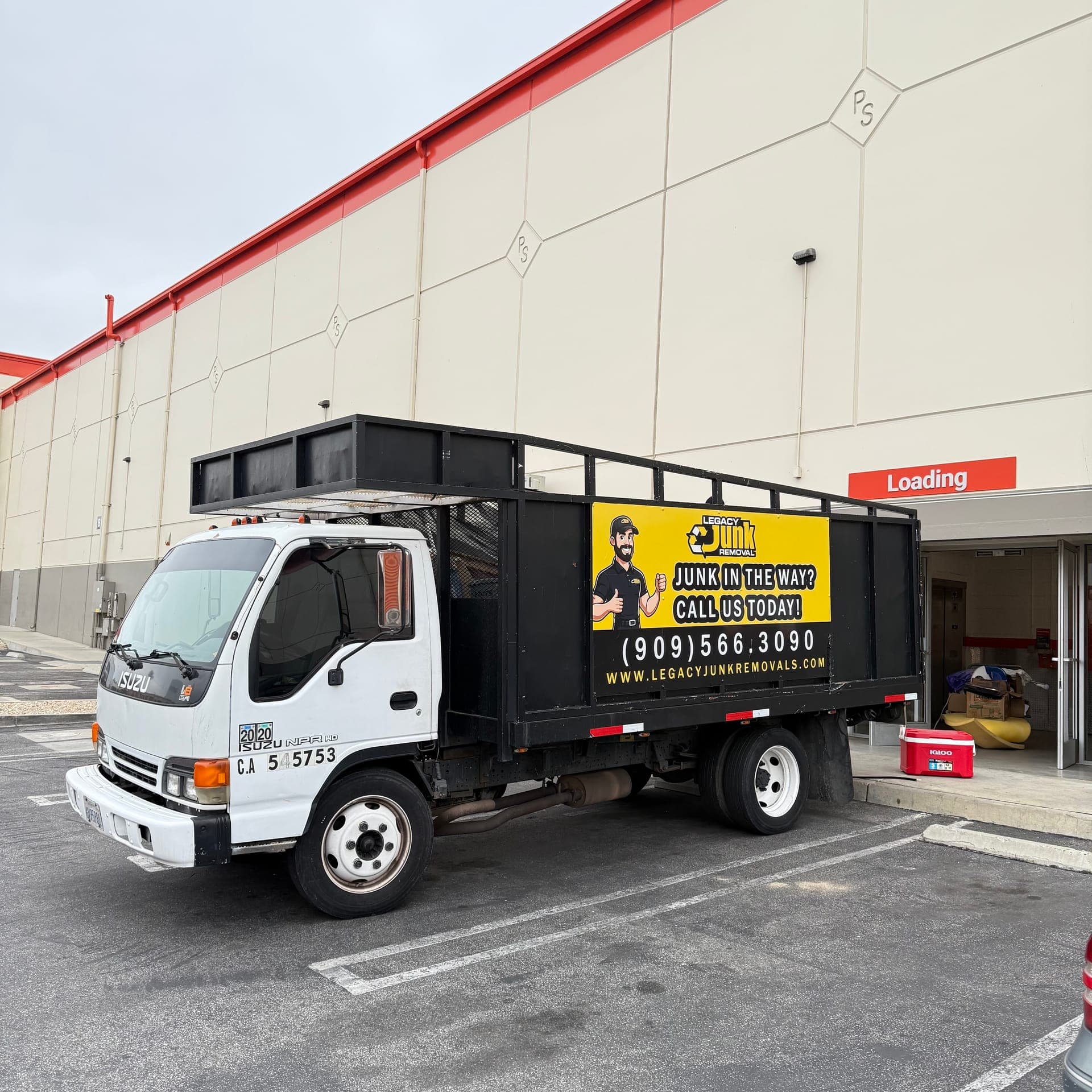 Legacy's white cab-over truck with its yellow and black wrap, parked at a loading door