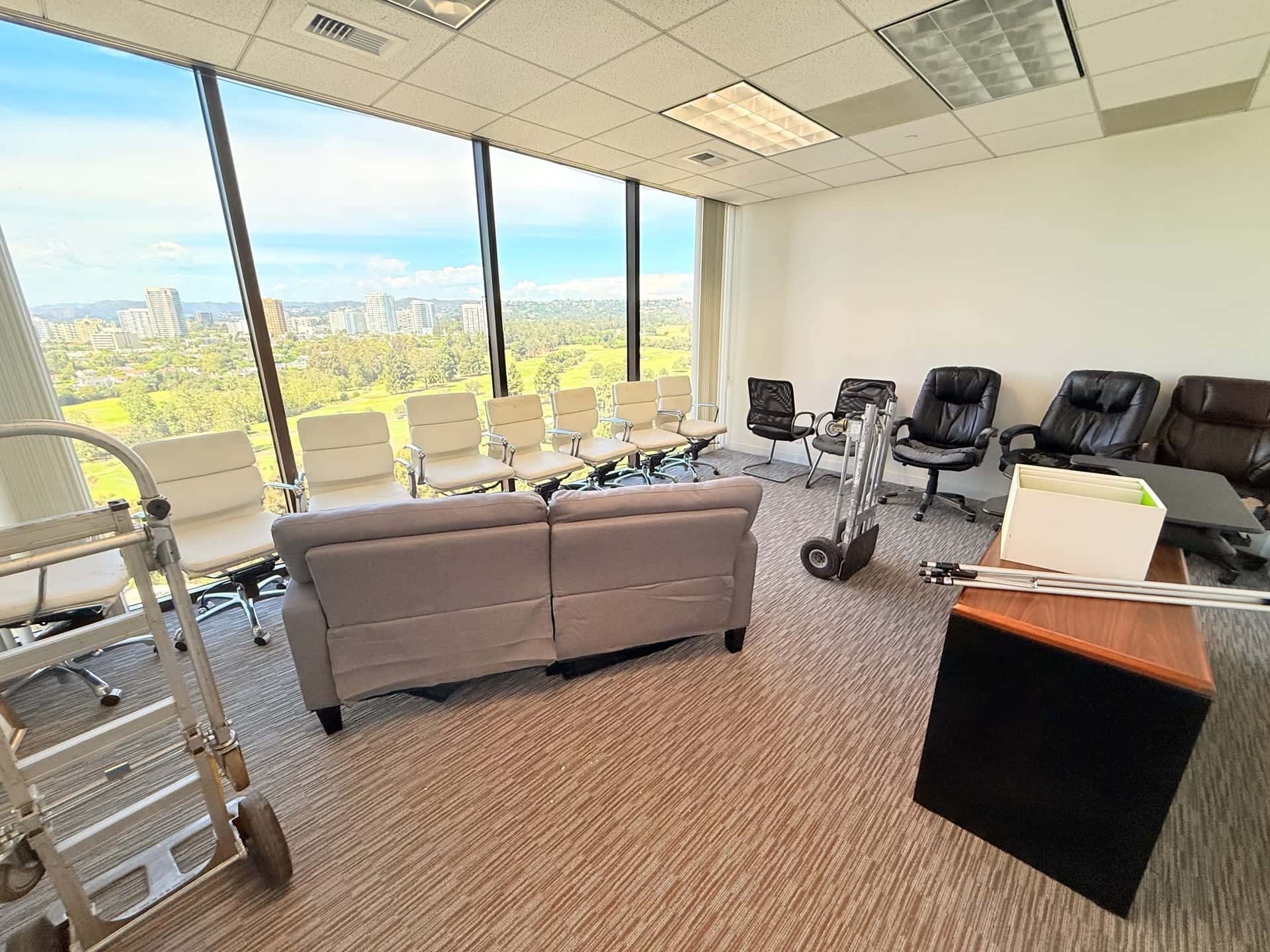 Before: office chairs, a sofa and a desk in a high-rise office, with a hand truck ready to move them