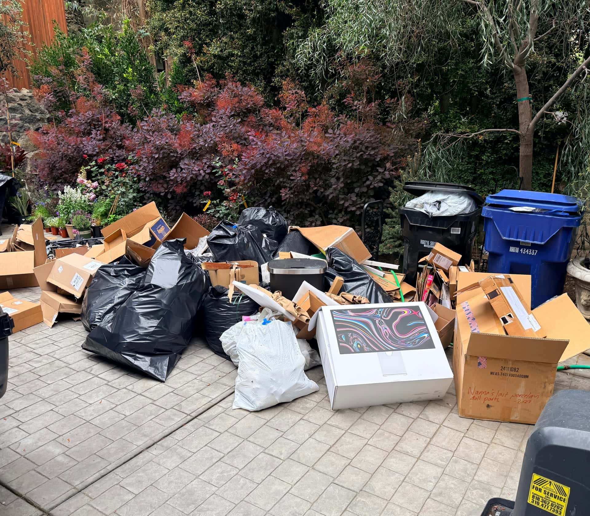 Before: flattened boxes and black trash bags piled on a paver patio by the garden