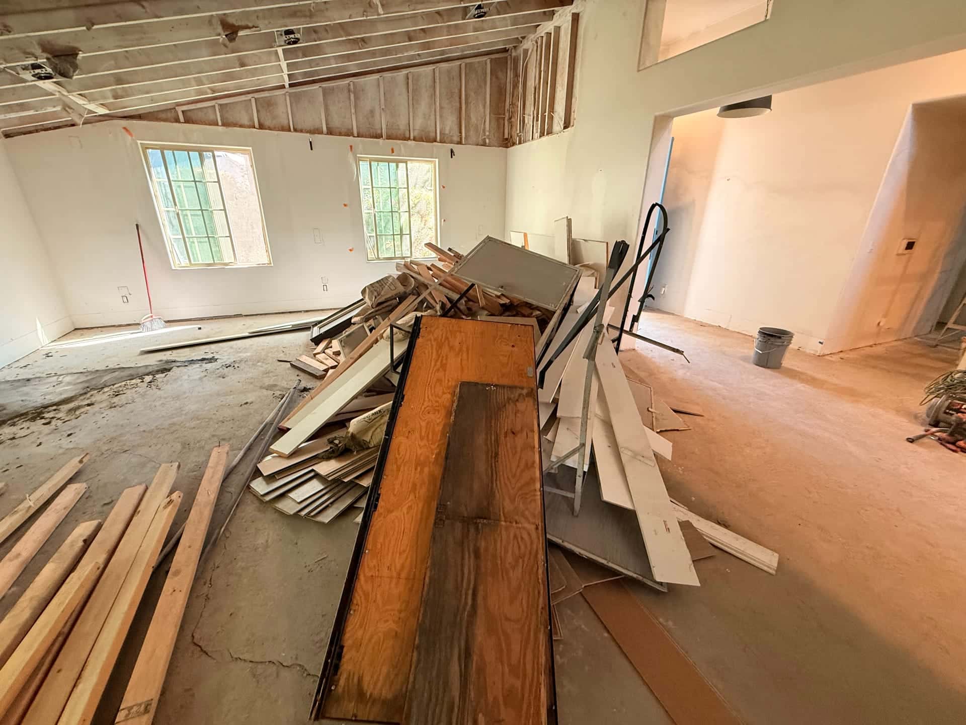Before: lumber, trim and old cabinet panels piled in a gutted room during a remodel