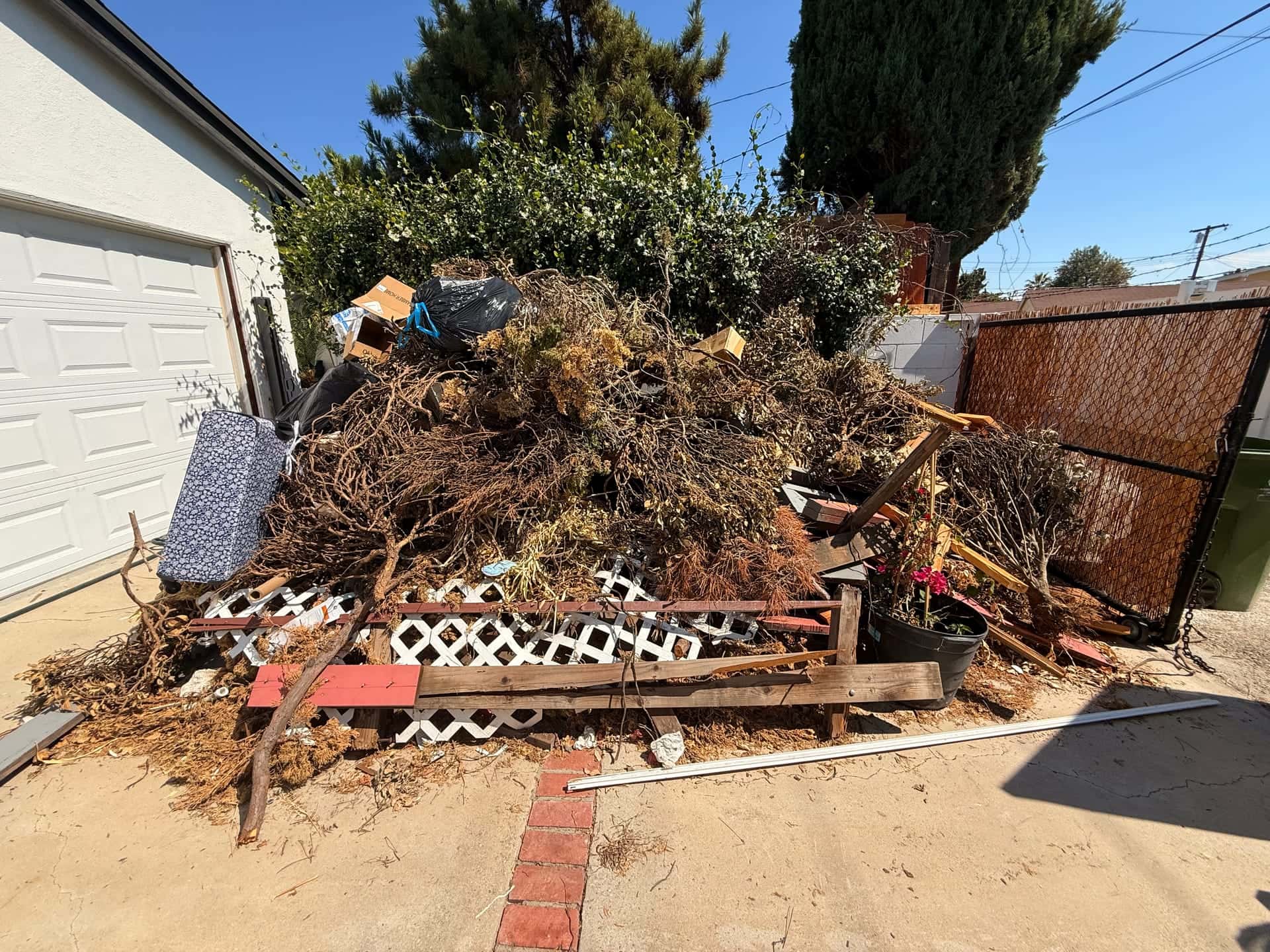 Before: a tall pile of branches, lattice and yard debris beside a garage